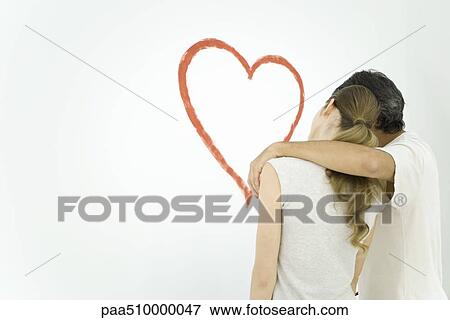 Stock Photo - Rear view of couple standing and looking at heart painted on wall. Fotosearch