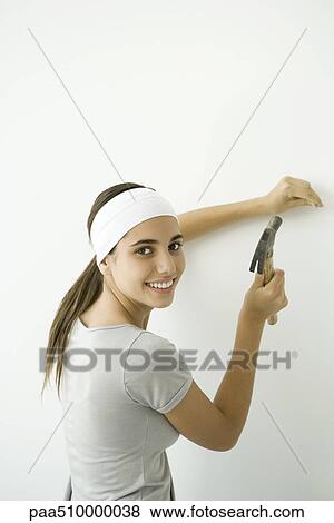 Stock Photo - Teen girl hammering nail into wall, smiling over her shoulder at camera. Fotosearch