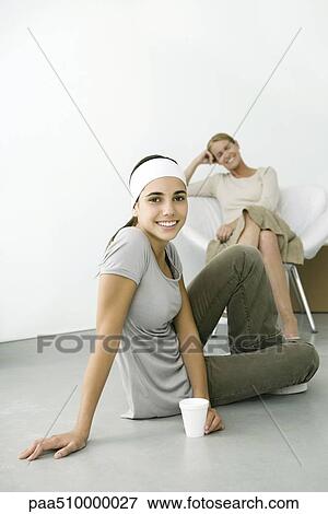Teen girl sitting on the ground with drink, smiling at camera, mother sitting in background View Large Photo Image Stock Photo - Teen girl sitting on the ground with drink, smiling at camera, mother sitting in background. Fotosearch