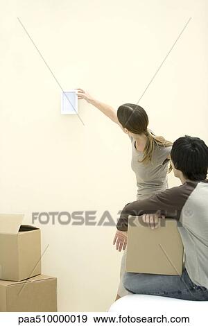 Woman hanging picture frame on wall, man watching, holding cardboard box View Large Photo Image Stock Photo - Woman hanging picture frame on wall, man watching, holding cardboard box. Fotosearch