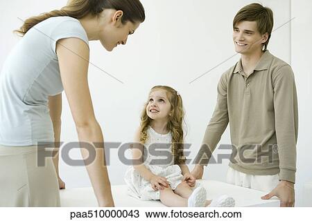 Stock Image - Young parents holding table, daughter sitting on table, smiling. Fotosearch