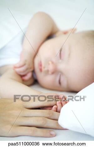 Stock Photograph - Adult holding sleeping baby's hand, cropped view. Fotosearch
