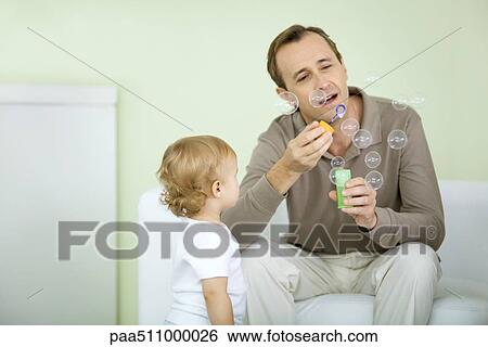 Stock Photograph - Father and toddler blowing bubbles together. Fotosearch