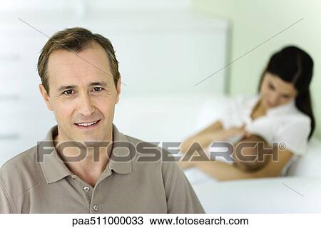 Mature man smiling at camera, wife nursing baby in background View Large Photo Image Stock Image - Mature man smiling at camera, wife nursing baby in background. Fotosearch