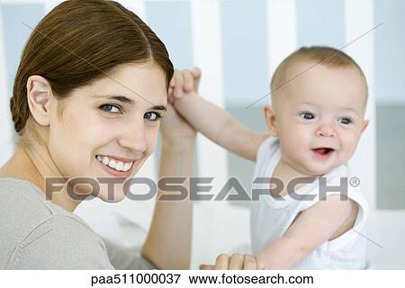 Stock Photo - Mother holding baby's hands and smiling at camera. Fotosearch