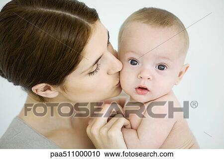 Stock Image - Mother kissing infant on the cheek, baby looking at camera. Fotosearch