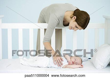 Mother leaning over side of crib to check sleeping infant View Large Photo Image Picture - Mother leaning over side of crib to check sleeping infant. Fotosearch