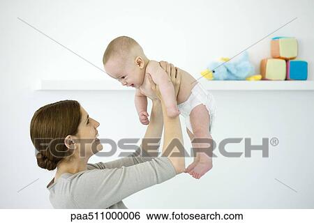 Stock Photograph - Mother lifting baby in the air, both smiling at each other. Fotosearch
