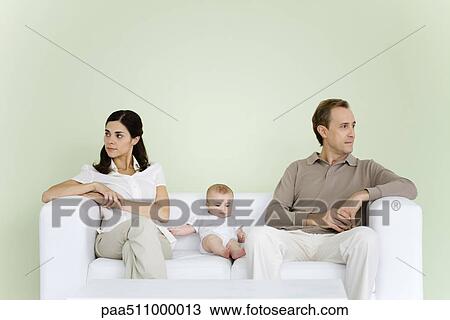 Pareja Sentar Sofa Con Bebe Entre Ellos Ambos El Mirar Lejos Coleccion De Imagen Paa Fotosearch