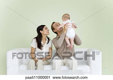 Parents sitting together on sofa, man holding baby View Large Photo Image Stock Image - Parents sitting together on sofa, man holding baby. Fotosearch