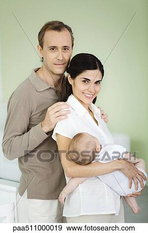 Parents smiling at camera, woman holding baby, portrait View Large Photo Image Stock Photo - Parents smiling at camera, woman holding baby, portrait. Fotosearch