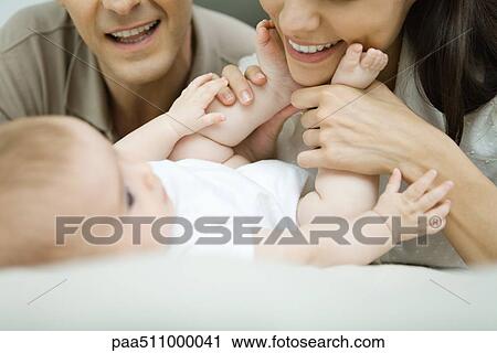 Parents smiling down at baby, mother holding baby's feet, cropped view View Large Photo Image Stock Image - Parents smiling down at baby, mother holding baby's feet, cropped view. Fotosearch
