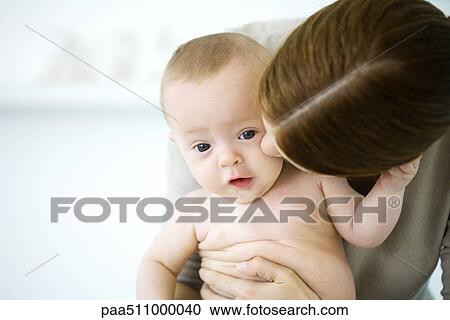 Stock Image - Woman kissing baby's cheek, baby looking at camera. Fotosearch