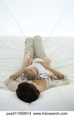 Picture - Woman lying on bed, holding infant on her stomach, rear view. Fotosearch