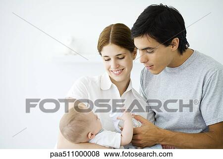 Young parents smiling down at baby, father helping baby hold bottle View Large Photo Image Stock Photo - Young parents smiling down at baby, father helping baby hold bottle. Fotosearch