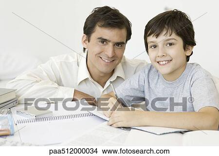 Boy doing homework with father, both smiling at camera View Large Photo Image Picture - Boy doing homework with father, both smiling at camera. Fotosearch