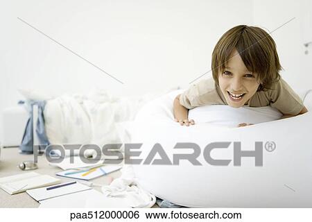Boy lying on stomach in messy room, smiling at camera View Large Photo Image Stock Photograph - Boy lying on stomach in messy room, smiling at camera. Fotosearch