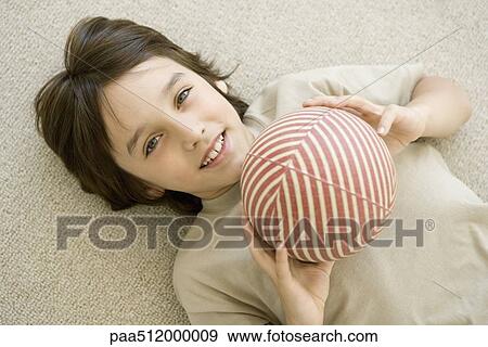 Boy lying on the ground, holding ball, smiling at camera View Large Photo Image Stock Photo - Boy lying on the ground, holding ball, smiling at camera. Fotosearch