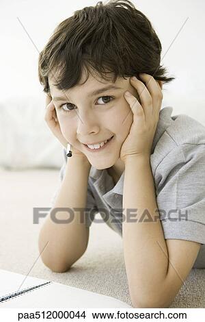 Boy lying on the ground with notebook, holding head, smiling at camera View Large Photo Image Picture - Boy lying on the ground with notebook, holding head, smiling at camera. Fotosearch