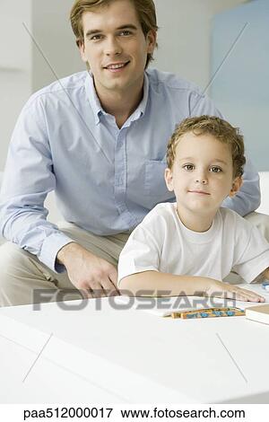 Stock Photo - Father and son sitting together with book, both smiling at camera. Fotosearch