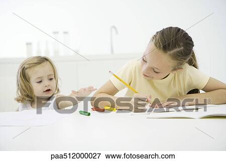 Girl doing homework at table, younger sister reaching for crayons View Large Photo Image Stock Photo - Girl doing homework at table, younger sister reaching for crayons. Fotosearch