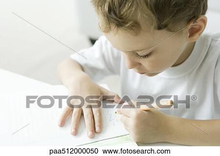 Stock Image - Little boy sitting at table, drawing with colored pencil. Fotosearch