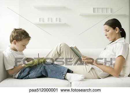 Mother and son sitting face to face on sofa, woman reading, boy writing in book View Large Photo Image Stock Image - Mother and son sitting face to face on sofa, woman reading, boy writing in book. Fotosearch