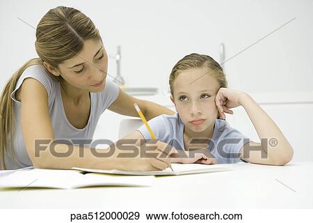 Stock Photo - Mother helping daughter with homework, girl looking away and sulking. Fotosearch