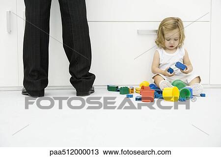 Toddler girl sitting on the ground beside father's legs, playing with toys View Large Photo Image Stock Image - Toddler girl sitting on the ground beside father's legs, playing with toys. Fotosearch