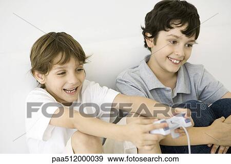 Stock Photo - Two boys playing video game together, one holding controller, both smiling. Fotosearch