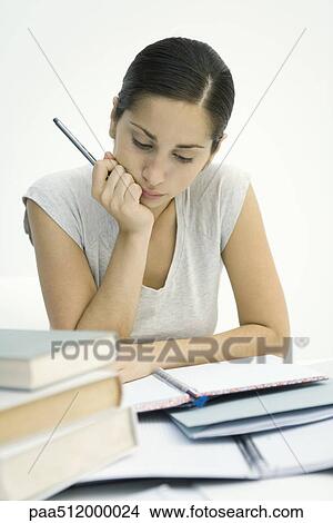 Picture - Young woman sitting with stack of books, studying notebook. Fotosearch