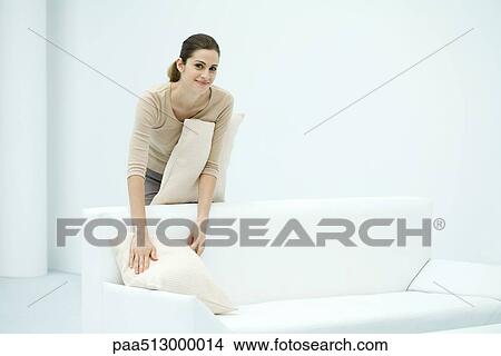 Woman arranging pillows on sofa, smiling at camera View Large Photo Image Picture - Woman arranging pillows on sofa, smiling at camera. Fotosearch