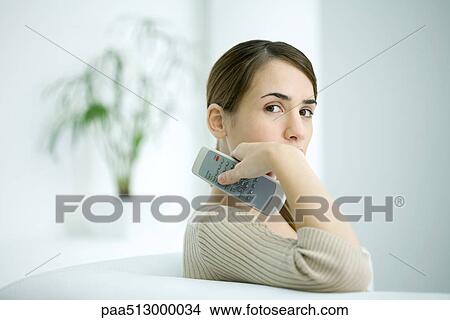 Woman holding remote control, looking over shoulder at camera View Large Photo Image Picture - Woman holding remote control, looking over shoulder at camera. Fotosearch