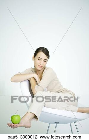 Woman lounging in chair, balancing apple on foot View Large Photo Image Stock Image - Woman lounging in chair, balancing apple on foot. Fotosearch