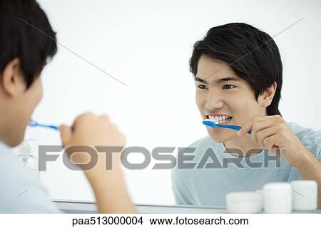 Young man brushing teeth, looking at self in mirror View Large Photo Image Picture - Young man brushing teeth, looking at self in mirror. Fotosearch