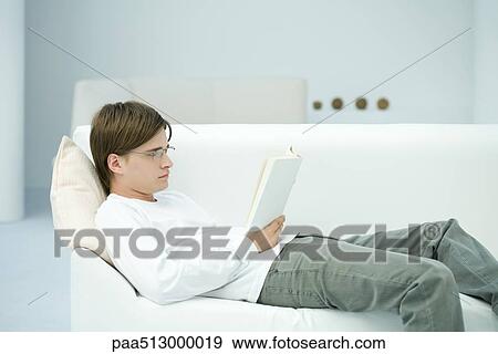 Stock Photograph Of Young Man Reclining On Sofa Reading Book Side Stock Photograph Young Man Reclining On Sofa Reading Book Side View Fotosearch