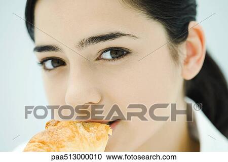 Stock Image - Young woman eating croissant, close-up. Fotosearch