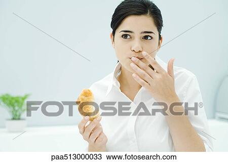 Young woman holding croissant, other hand in front of mouth View Large Photo Image Stock Image - Young woman holding croissant, other hand in front of mouth. Fotosearch