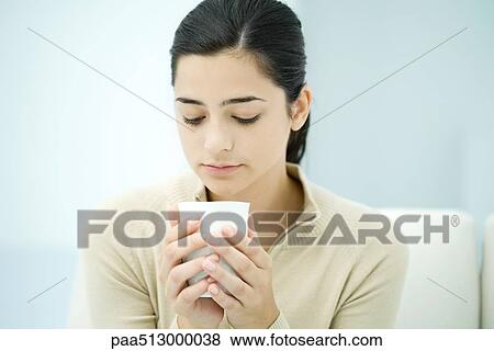 Young woman holding cup, looking down View Large Photo Image Stock Photo - Young woman holding cup, looking down. Fotosearch