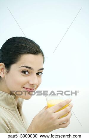 Stock Image - Young woman holding glass of orange juice, smiling at camera. Fotosearch