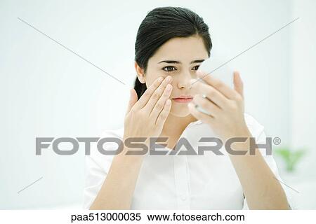 Young woman looking at self in hand mirror, touching her cheek View Large Photo Image Stock Photography - Young woman looking at self in hand mirror, touching her cheek. Fotosearch