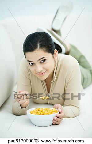 Young woman lying on stomach, eating bowl of cereal View Large Photo Image Stock Image - Young woman lying on stomach, eating bowl of cereal. Fotosearch