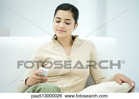 Young woman sitting on sofa, listening to MP3 player View Large Photo Image Stock Photograph - Young woman sitting on sofa, listening to MP3 player. Fotosearch