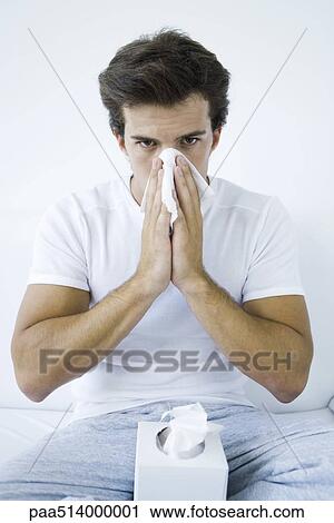 Stock Image - Man blowing his nose with a tissue, looking at camera. Fotosearch