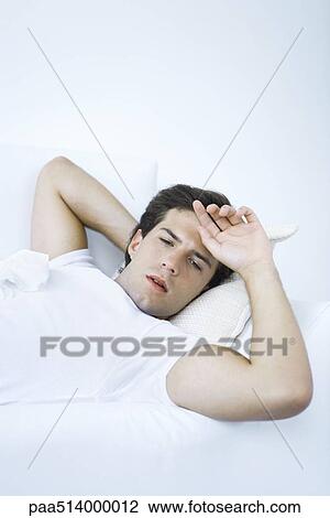 Stock Image - Man lying on sofa with tissue on his chest, hand on forehead. Fotosearch