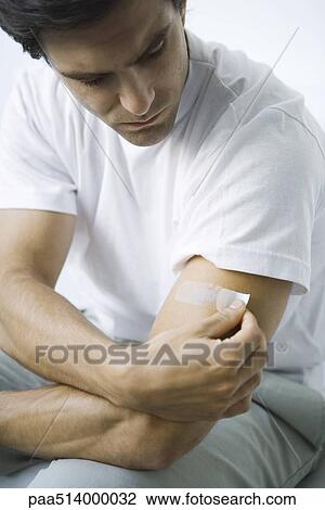 Stock Image - Man putting adhesive bandage on his arm. Fotosearch