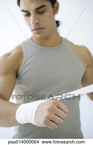 Picture - Man wrapping bandage around his wrist, looking down. Fotosearch