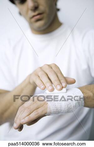 Stock Photograph - Man wrapping gauze around his wrist and hand, cropped view. Fotosearch