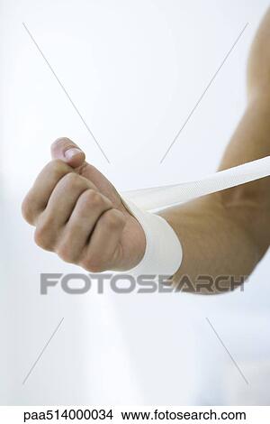 Picture - Man wrapping gauze around his wrist, cropped view. Fotosearch