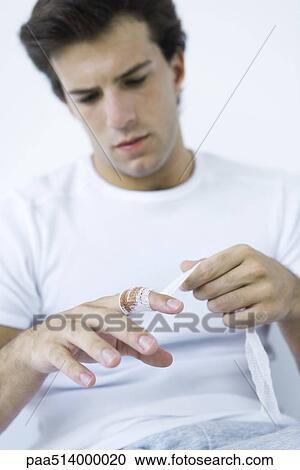 Stock Image - Man wrapping gauze around injured finger. Fotosearch